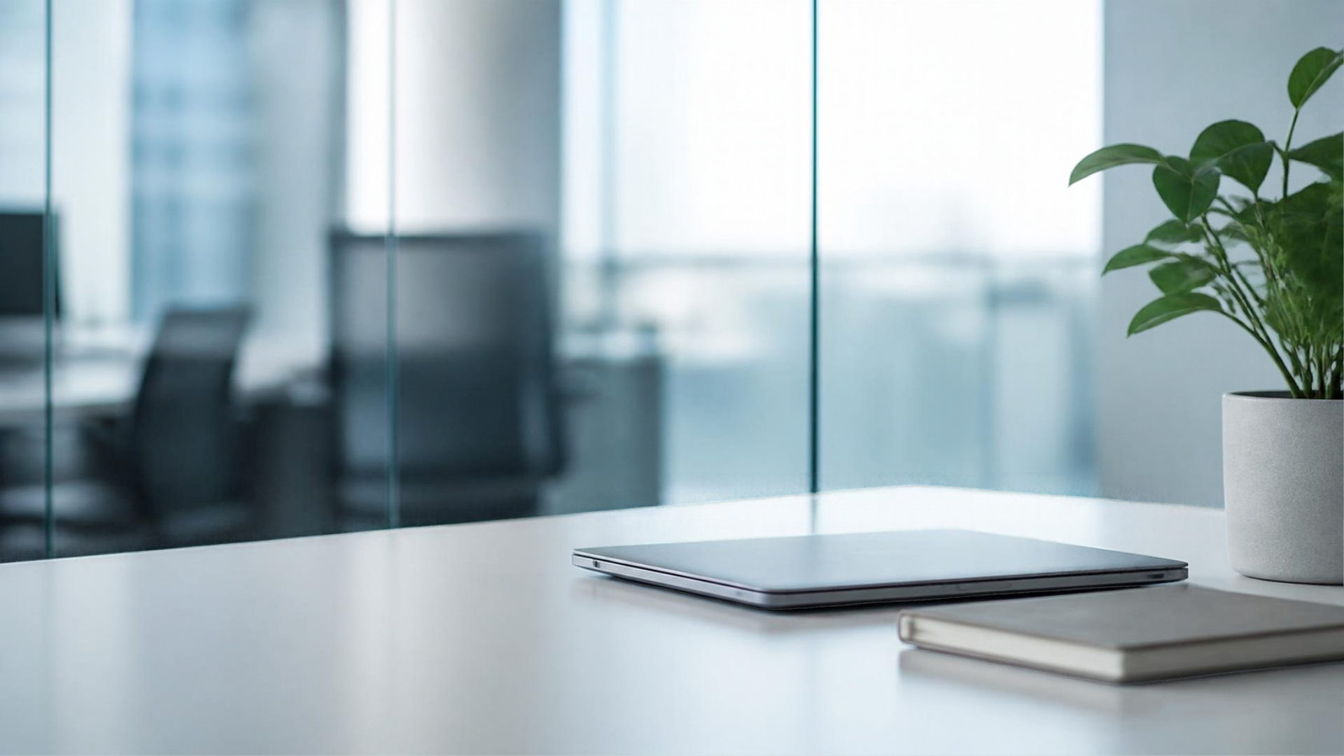 A calm modern office desk with a closed laptop beside a glass partition